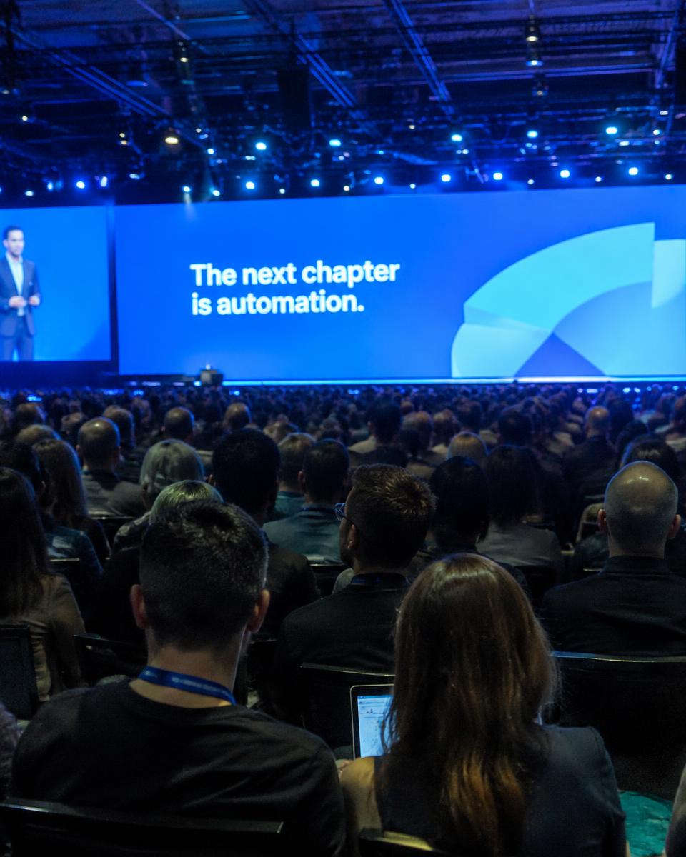 A conference audience facing a large keynote screen