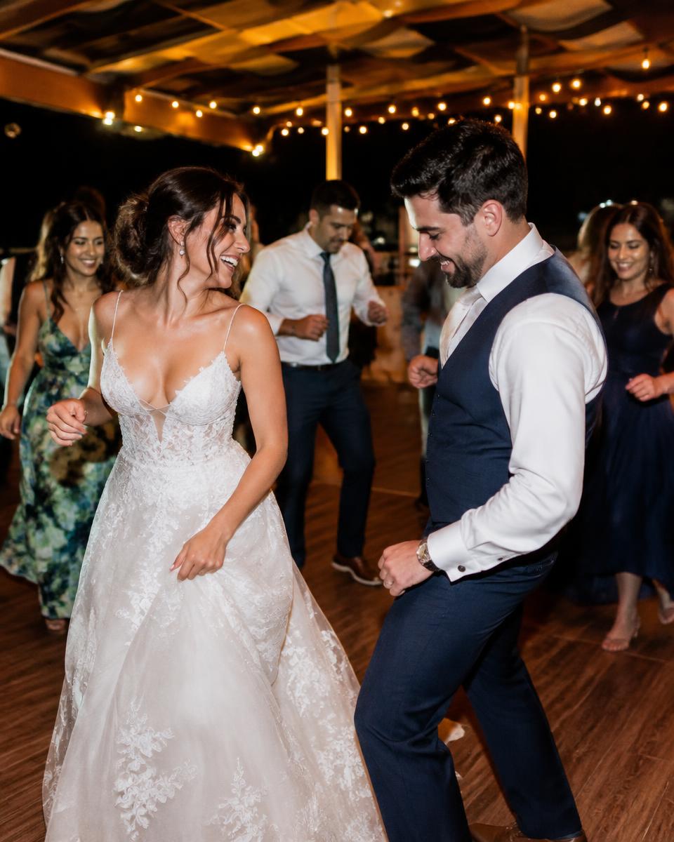 A bride and groom dancing with wedding guests under string lights